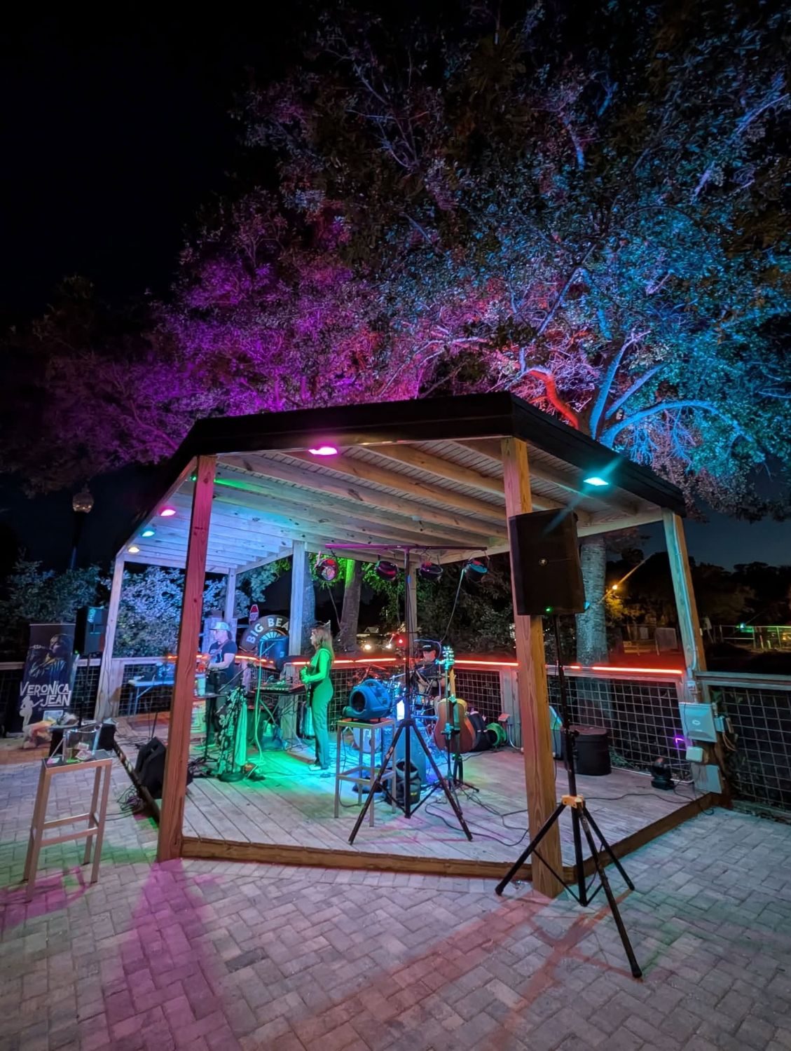 Live band performing under a pavilion lit with colorful stage and uplighting