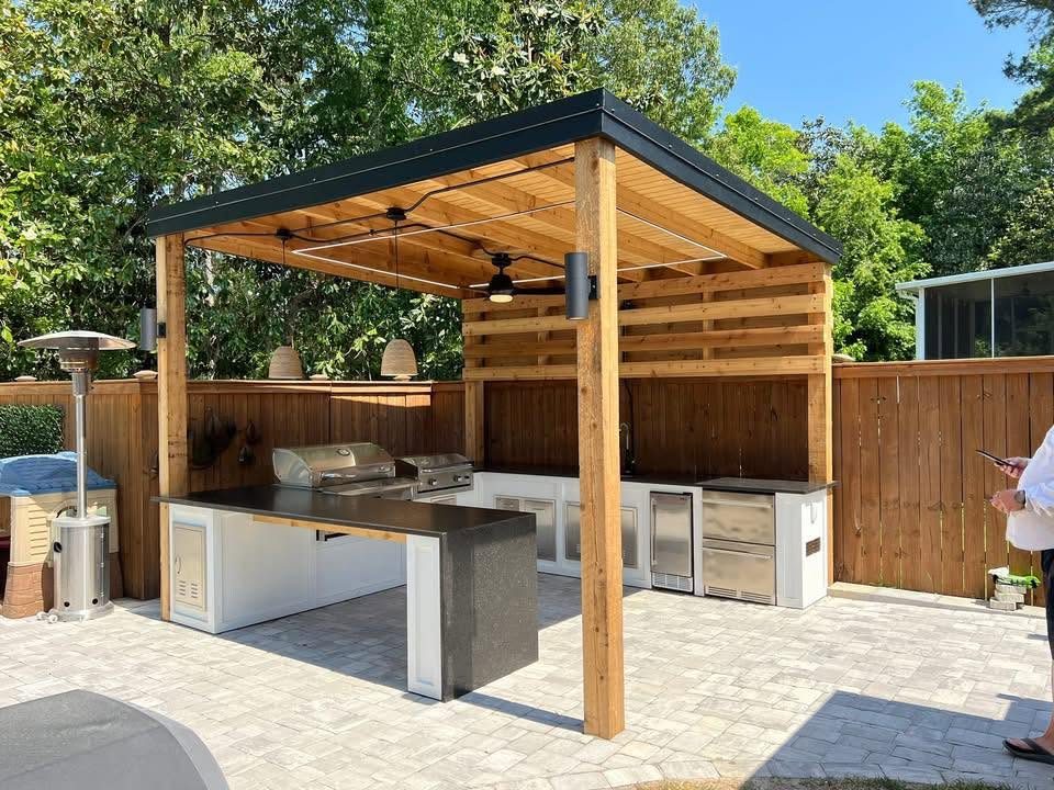 Finished outdoor kitchen under a cedar pergola with a black metal roof, wired for lighting, a fan, and appliances